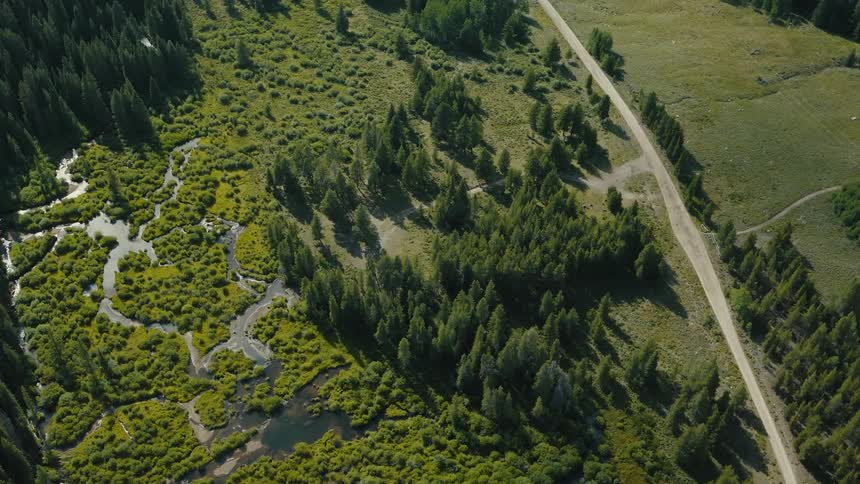 Aerial landscape shows a winding river between green areas and a dirt road