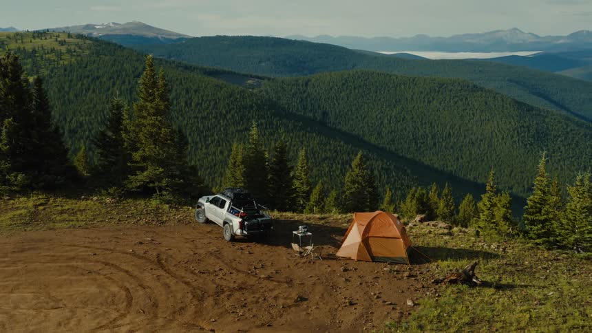 Orange tent and white suv at campsite set before forested mountains