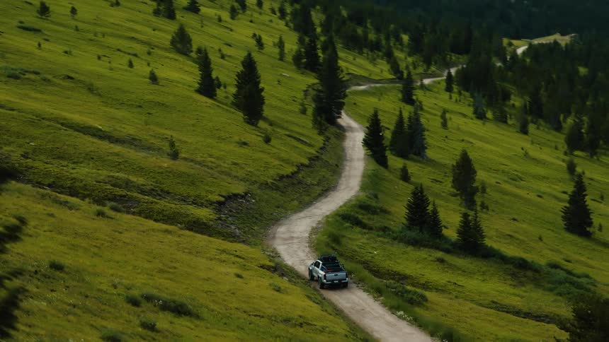 Pickup truck driving on a road surrounded by trees with a forest and mountain range on the background outdoors during day time