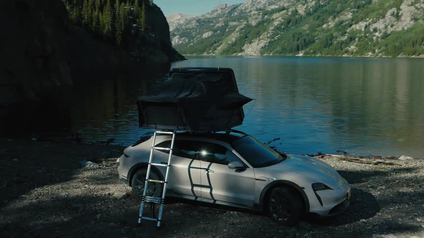 A camper is on top of the car by the lake
