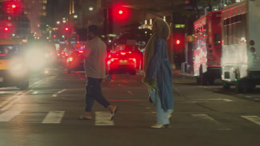 A female is walking briskly on a crosswalk in a busy city with many vehicles and people all around at night