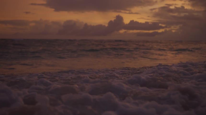 Waves roll into shore and over the beach under a colorful cloudy sky