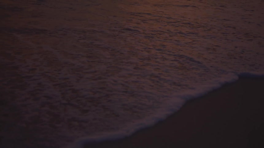 Dark waves roll gently over the stretch of sand at nightfall