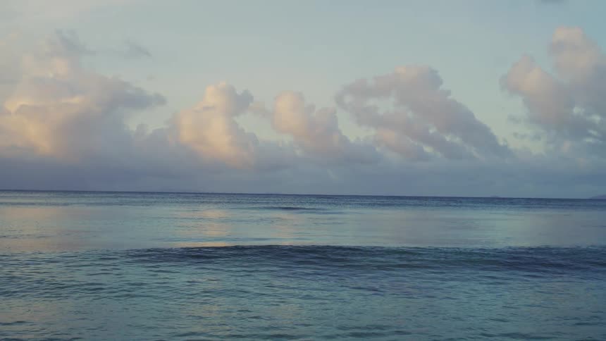 A calming view of the turquoise ocean ripples and low rolling waves beneath a cloudy sky with soft pink and orange hues at the horizon