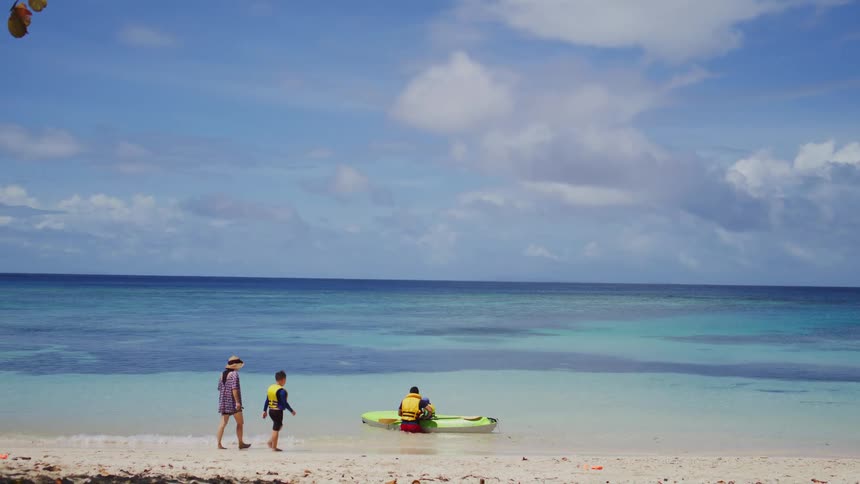 Two people walking towards another male person preparing an inflatable kayak at the beach outdoors during day time