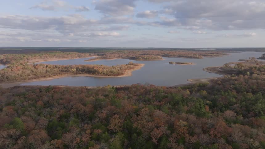 Lakes surrounded by mixed forest stretch across hills under partly cloudy sky