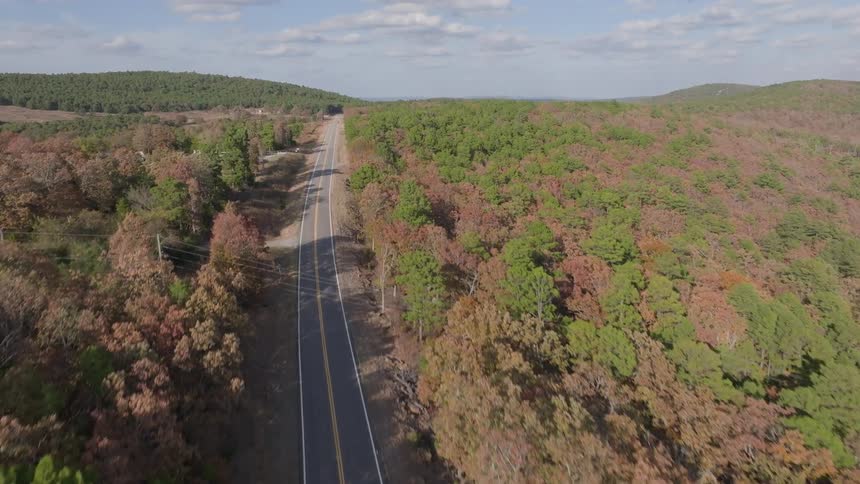 Straight road cuts through wooded hills with scattered buildings beside dense forest
