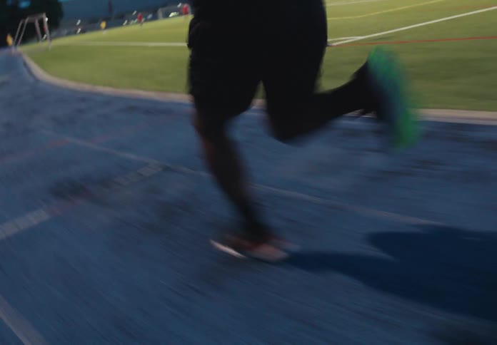 A low motionblurred shot follows an athletes legs as he runs quickly on a blue track then slows down to a jog before stopping at the edge of the running surface