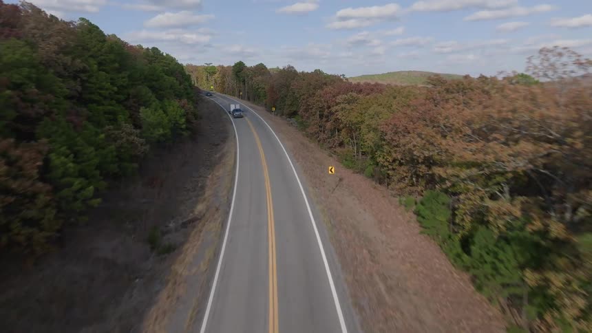 Aerial view of light traffic on a road curving around a forested mountain