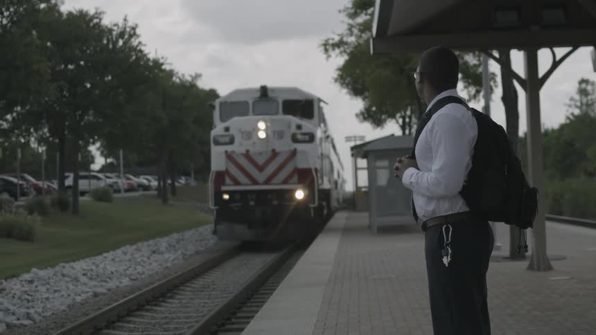 Man wearing a backpack looks at a train pulling into a station