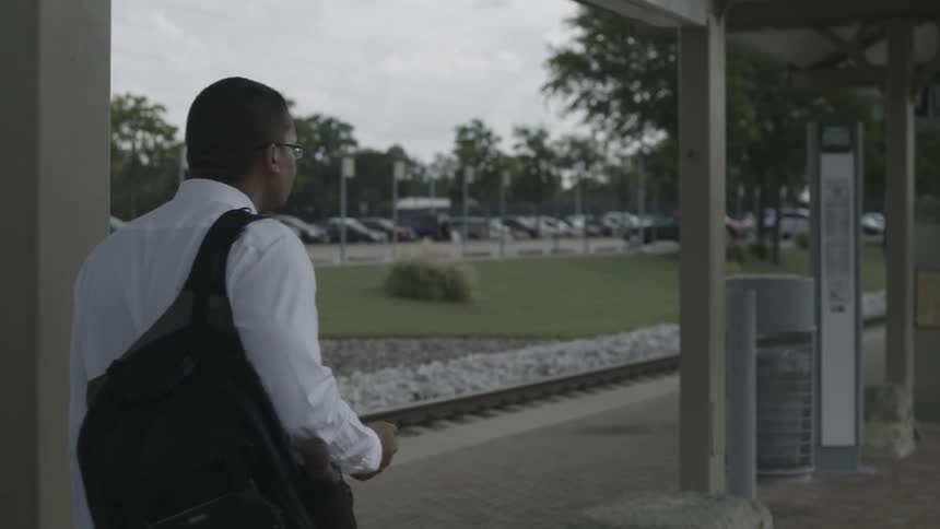 Man wearing backpack waits at a train station