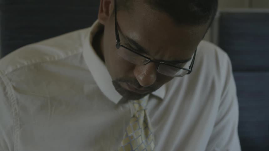 Person wearing a suit holds a pen while looking down at a binder