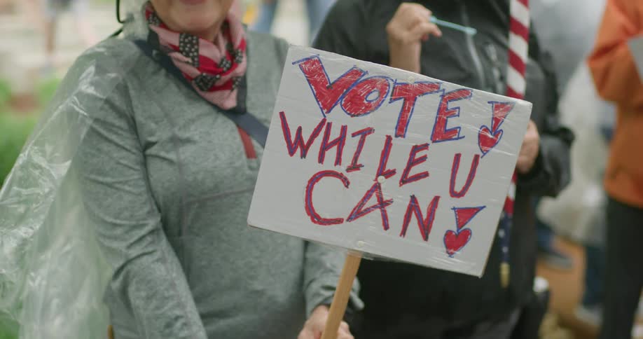 The woman is holding a sign that says vote while you can