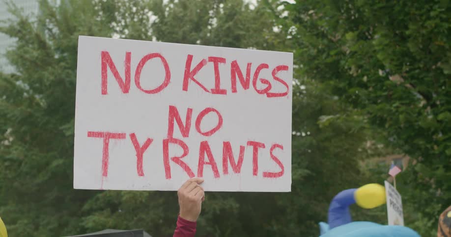 A person holds up a white protest sign reading no kings no tyrants in bold red letters