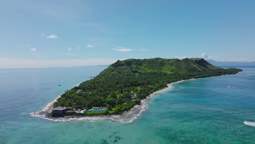 An aerial view captures a lush tropical island featuring a resort on its tip surrounded by turquoise waters