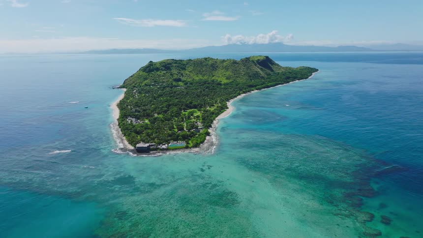 Tropical island with central hill is surrounded by white beaches reefs and clear blue sea