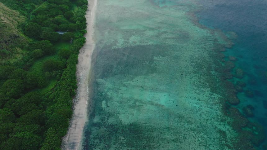 Dense greenery meets narrow beach and shallow reefs in tropical coast with turquoise waters