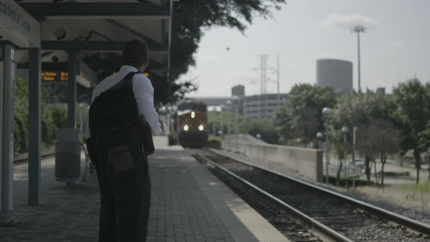 A man standing on a train platform waiting as the train comes into the station