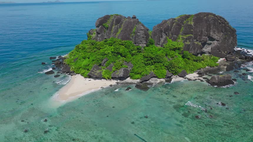 Tropical island with dense vegetation and rock formations surrounded by shallow turquoise waters