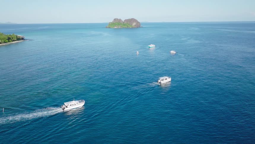 Multiple boats move through the blue waters at a distance from forest covered islands on a summer day