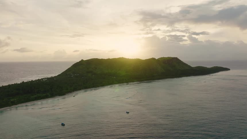Two boats are moving away from the green island