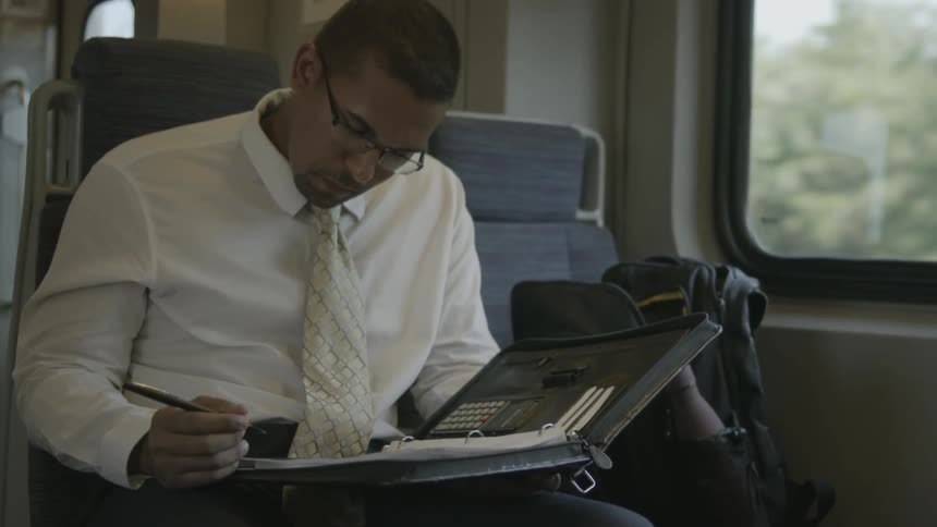 Man sits on a train writing in a binder