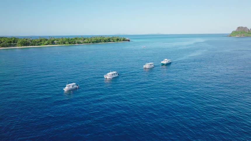 Boats lined up on the blue sea in front of a lush island