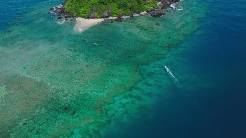 A boat glides across the ocean at midday heading toward a mountainous island rising in the distance
