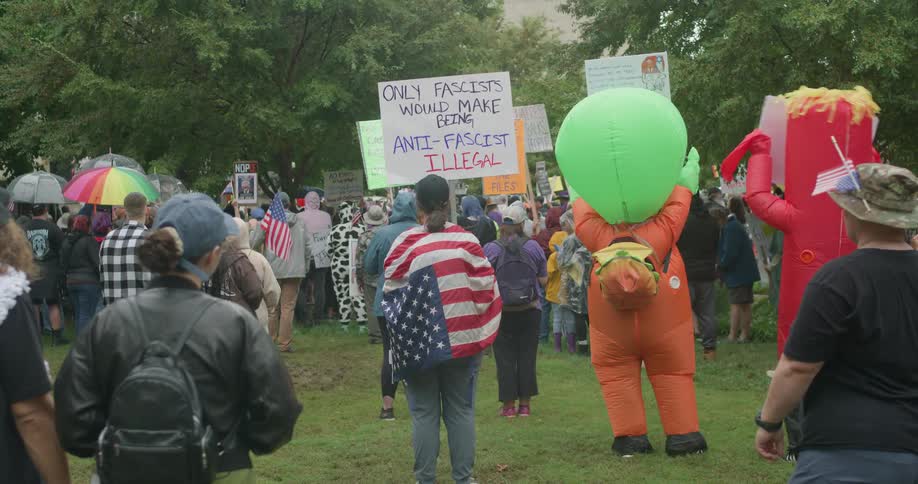 A crowd of protesters waving flags and boards at an outdoor protest in a city during daytime