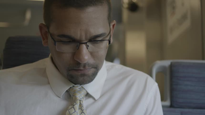 A man with glasses and a suit shirt is sitting at a desk or table looking down