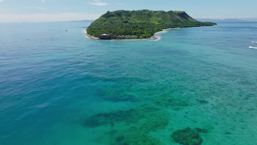 Tropical island surrounded by reefs and turquoise waters with shoreline structures and clear skies