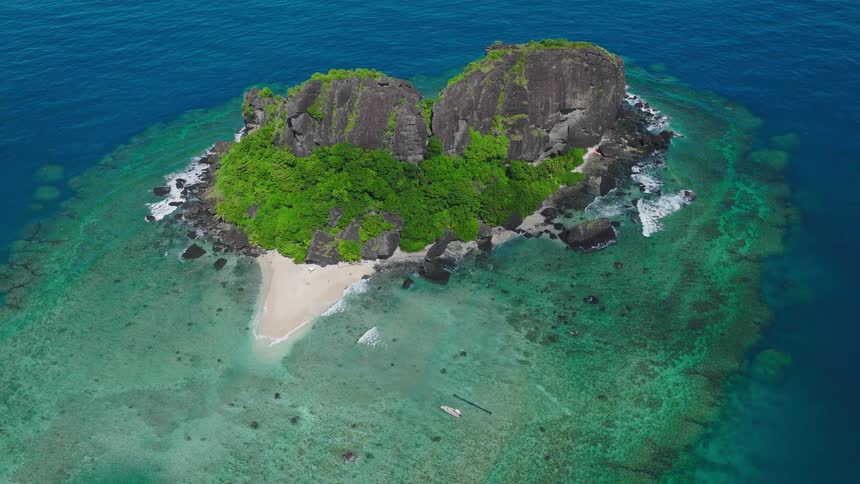 Tropical island surrounded by turquoise waters and coral reefs with boat anchored on sandy beach