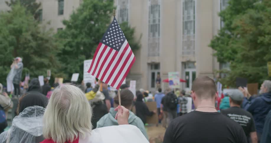 Crowd gathers in front of institutional building during protest with flags and signs