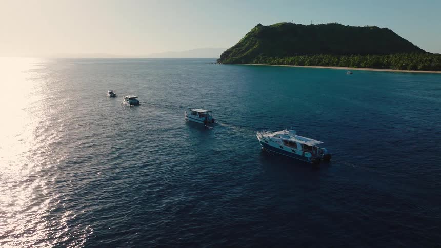 Aerial view of boats sailing toward a green island across a blue ocean