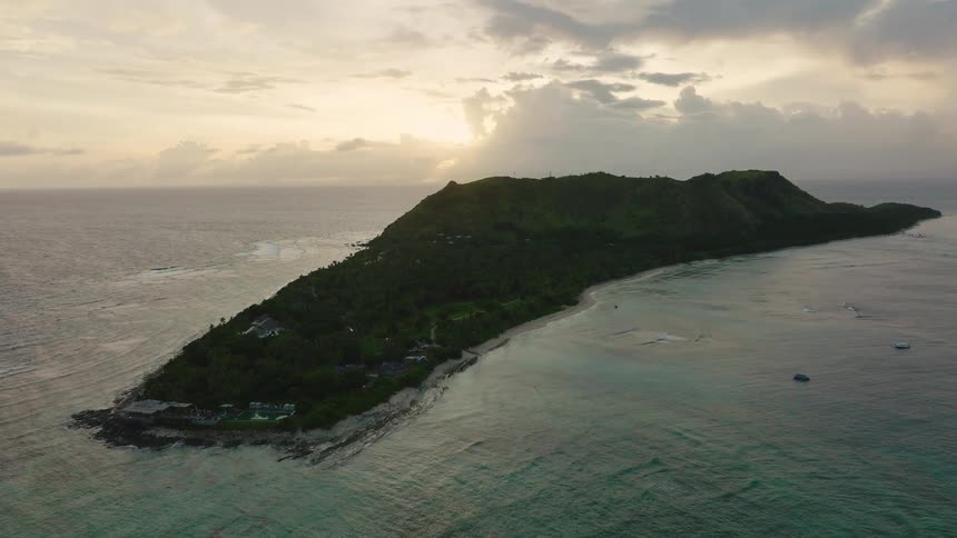Green mountainous island stretches into the sea under golden light of sunrise or sunset