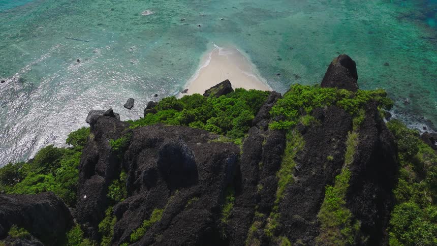 Jagged greencovered rock formations rise above reefs and turquoise waters near inhabited island