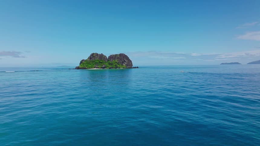Rocky island covered in green vegetation in clear blue ocean with bright sky in the background