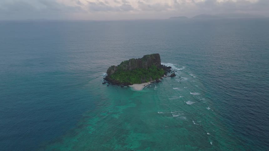 An aerial view of a small green island in turquoise water under a cloudy sky