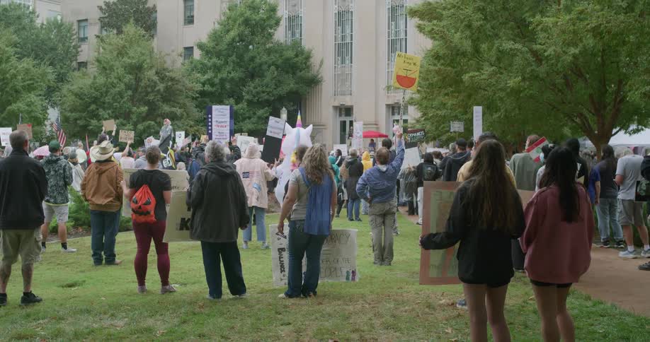 Protesters gathered outdoors holding signs in front of a public building
