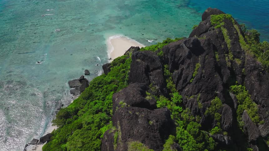 Rocky forested island rises from clear blue ocean waters seen from above
