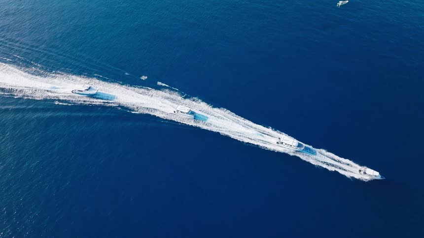 A series of boats race across the ocean at midday chasing one another and cutting through the waves