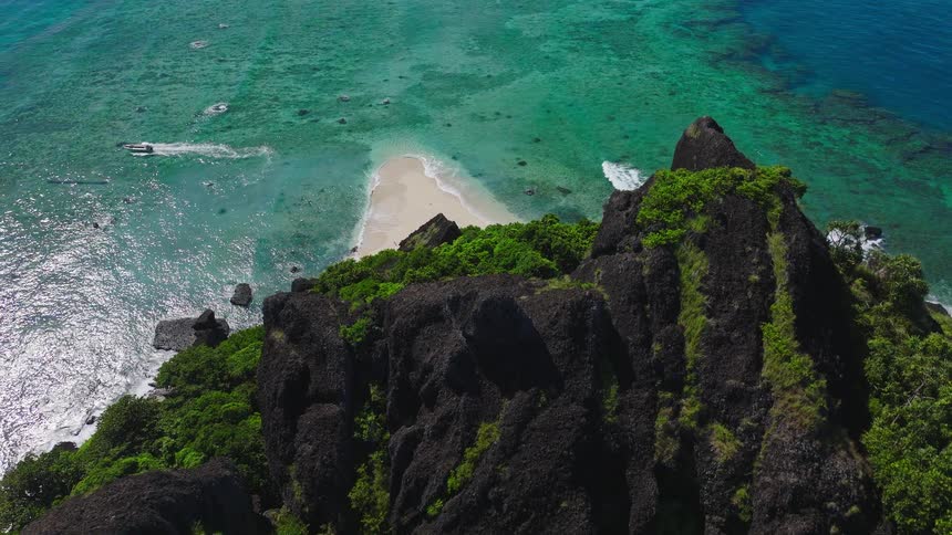 Tropical island with rocky hill covered in vegetation surrounded by turquoise waters and shallow beach