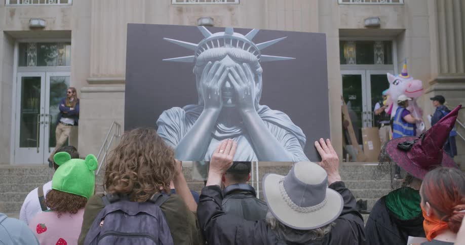 A group of people carrying a painting of the statue of liberty while standing outdoors during a demonstration in a metropolitan city during daytime