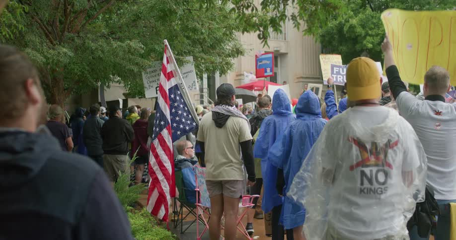 Crowd of people with signs and an american flag protesting in front of a building outdoors during day time