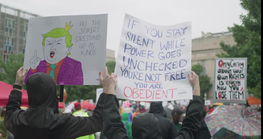 A group of protesters raising protest banners while at an outdoor demonstration in a metropolitan city on a rainy day