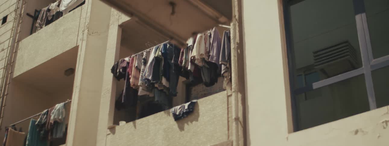 A residential building stands at midday with a series of clothes spread out across the balconies to dry in the sun