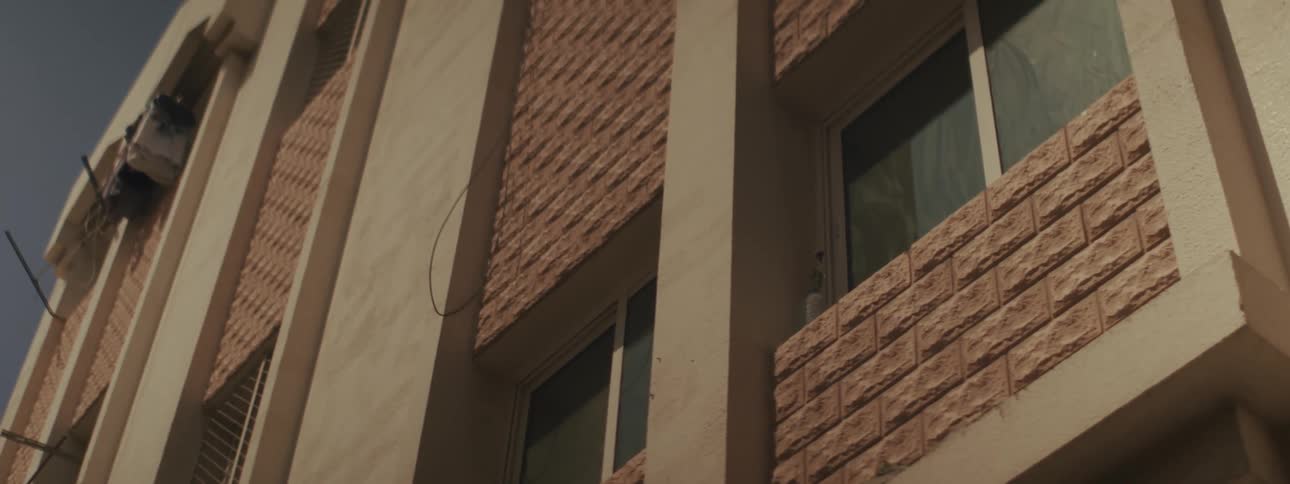 A close view of a modern building exterior showing columns separating stucco walls and sections of patterned brickwork surrounding windows