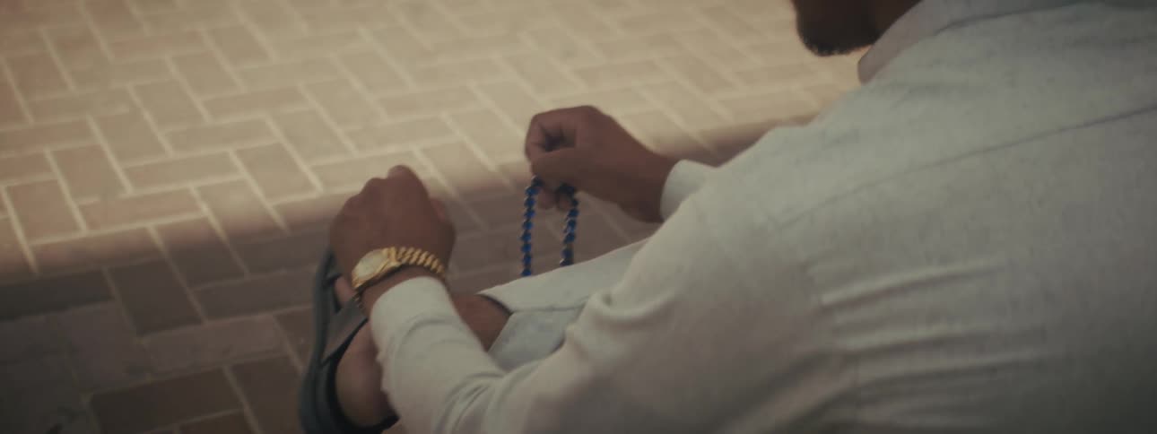 Close up of a young man praying with blue prayer beads while sitting outdoors at a walkway during daytime