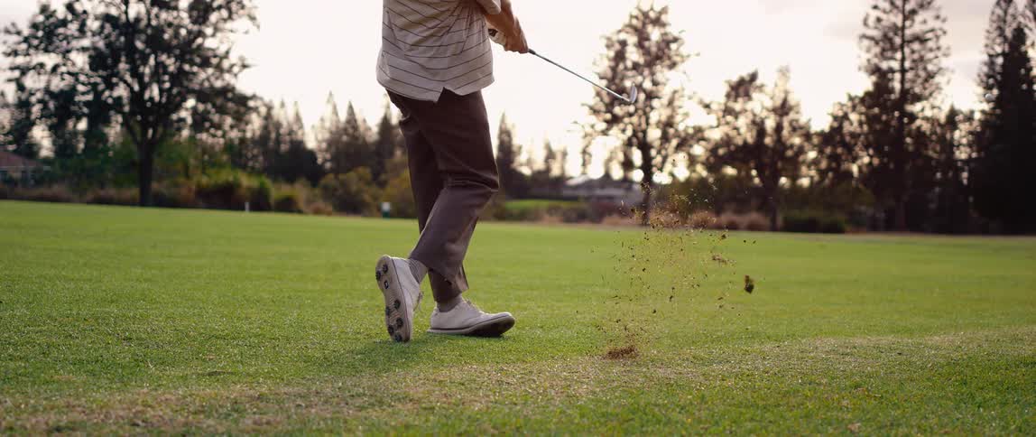 A golfer swings his golf club and hits a golf ball into the air
