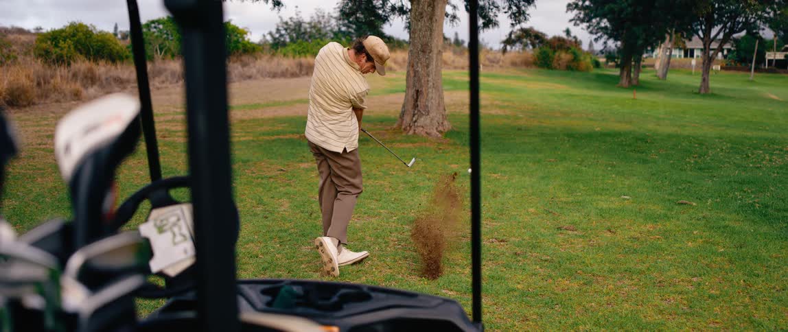 A man hits the golf ball with the club on the golf course at midday
